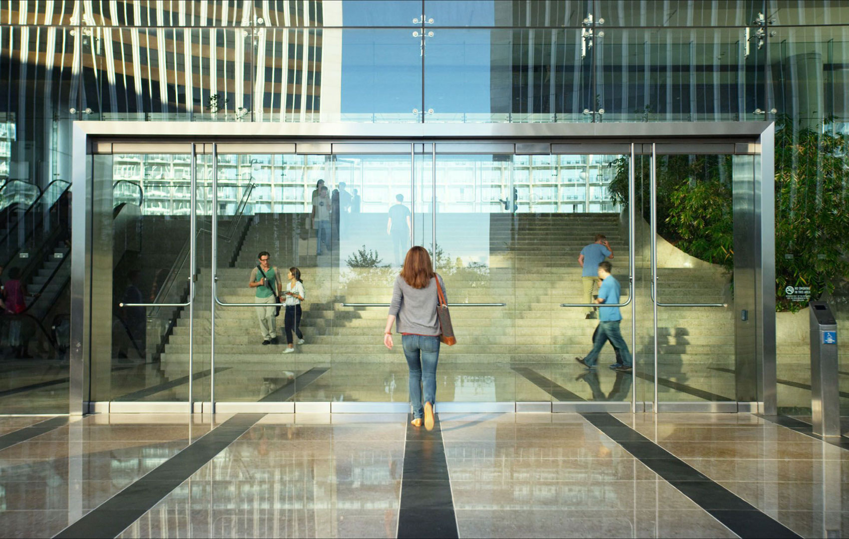 Eine Frau geht auf eine gläserene Tür zu, die zu einem verspiegelten Bürogebäude führt.