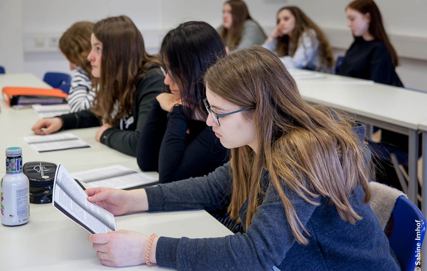 Schülerinnen sitzen an Tischen in einem Klassenraum und lesen einen Textauszug.