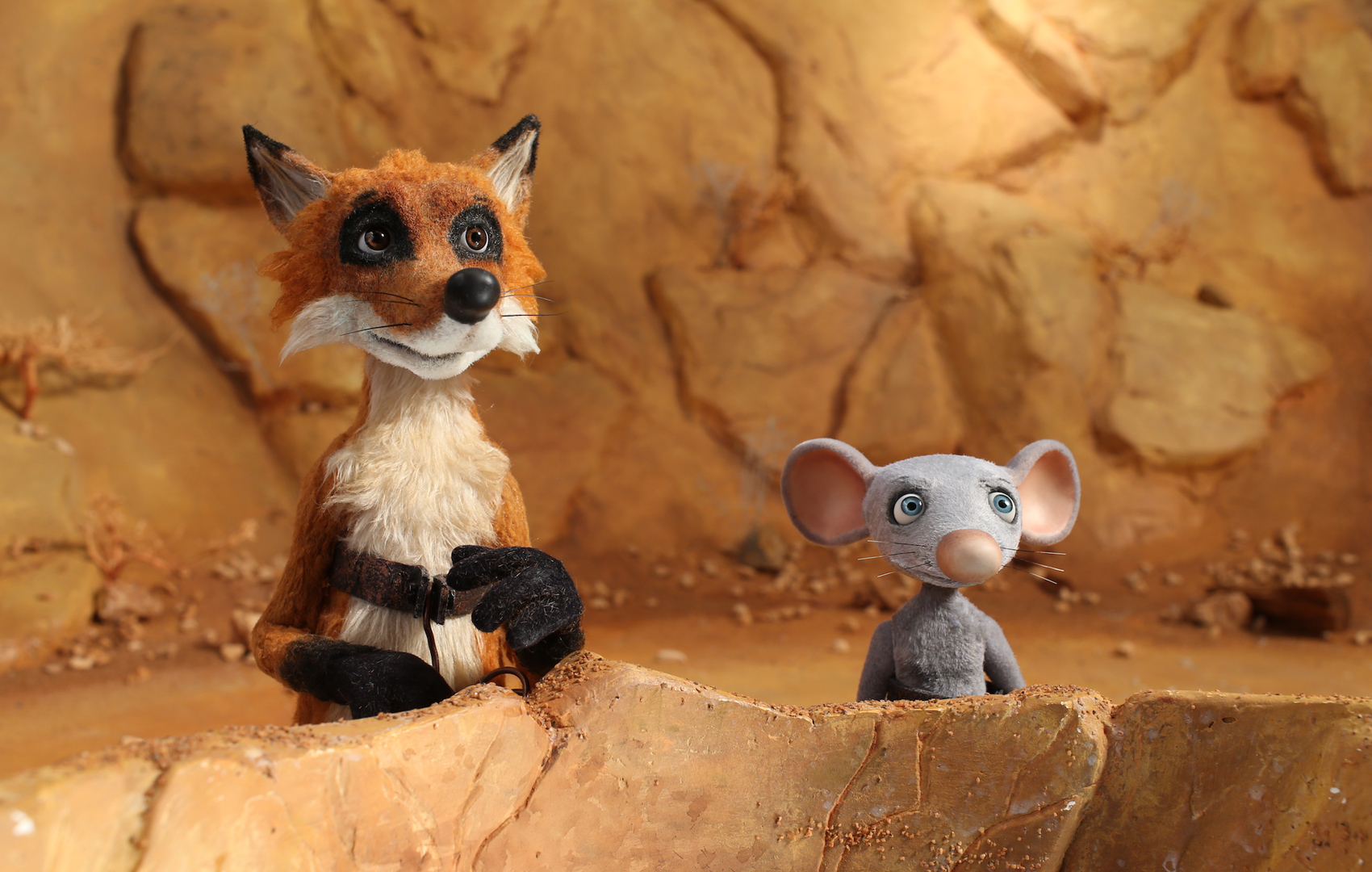 Puppentrick-Animation: Ein Fuchs steht neben einer Maus vor einem steinigen Wüstenhintergrund.