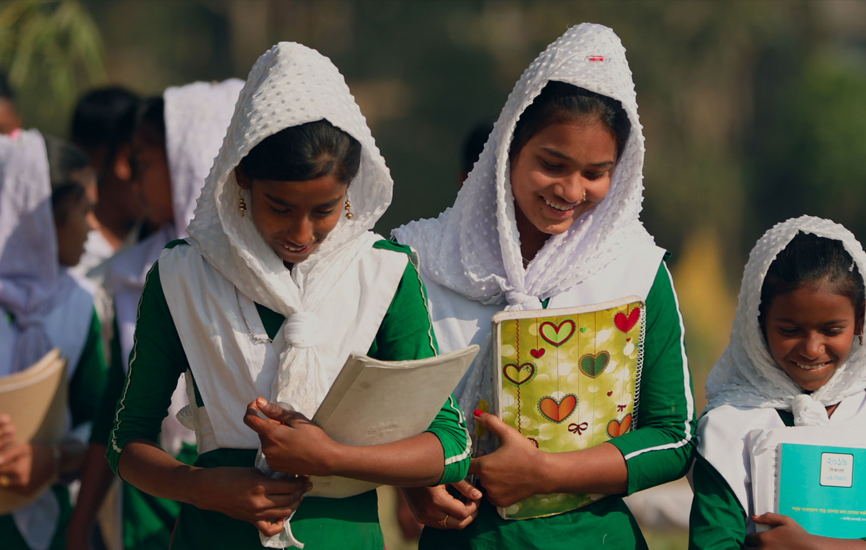 Lachende Mädchen mit Schulblöcken in der Hand. Sie kommen nicht aus Europa; zur Schuluniform gehören unter anderem weiße Kopftücher.