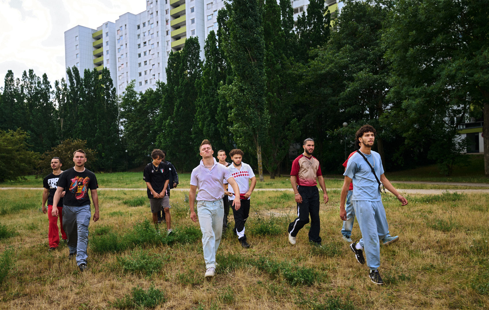 Junge Männer laufen in der Gruppe auf einer Wiese vor einer Hochhaussiedlung.