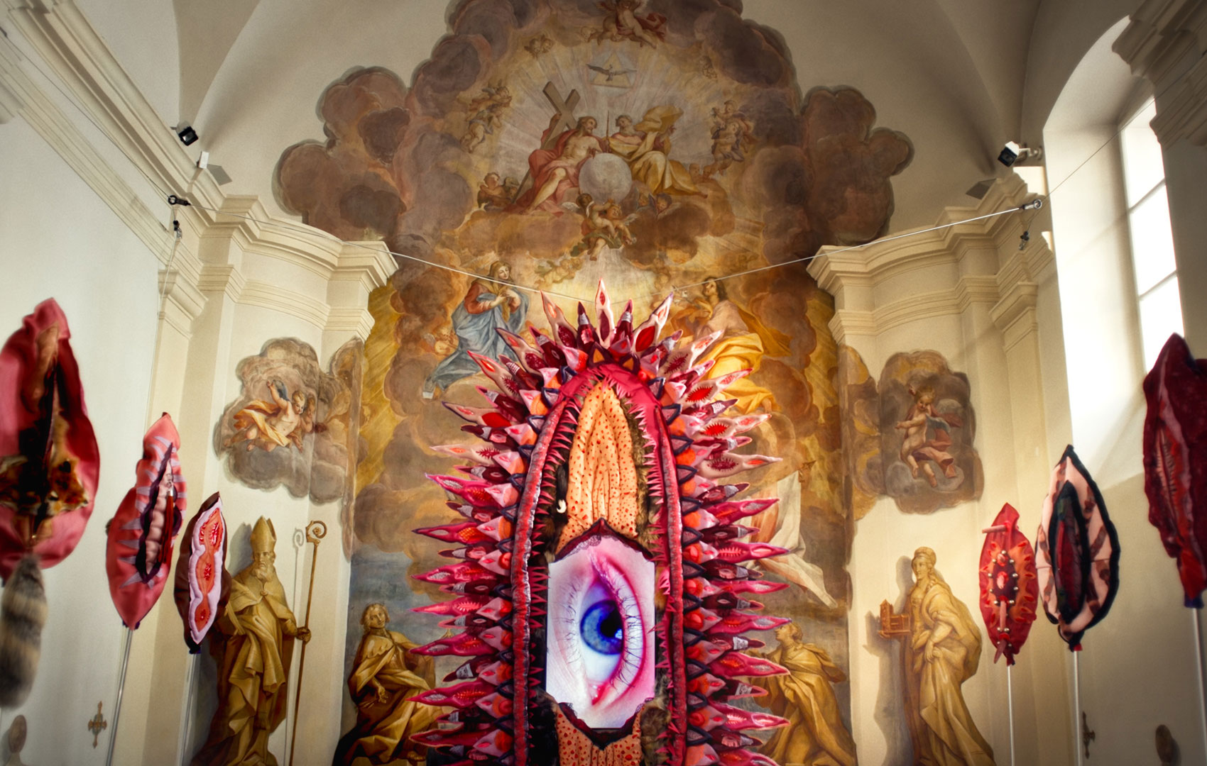 Kunstinstallationen in Form von Vulven in einem kirchlichen Altarraum vor einem dachhohen Fresko.