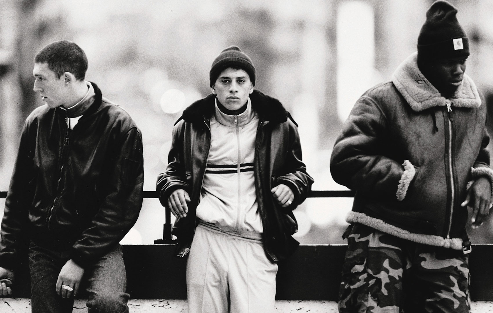 Schwarz-weiß Bild: Drei Jugendliche stehen nebeneinader. Die zwei äußeren schauen jeweils nach rechts und links aus dem Bild heraus, der mittelere schaut direkt in die Kamera.