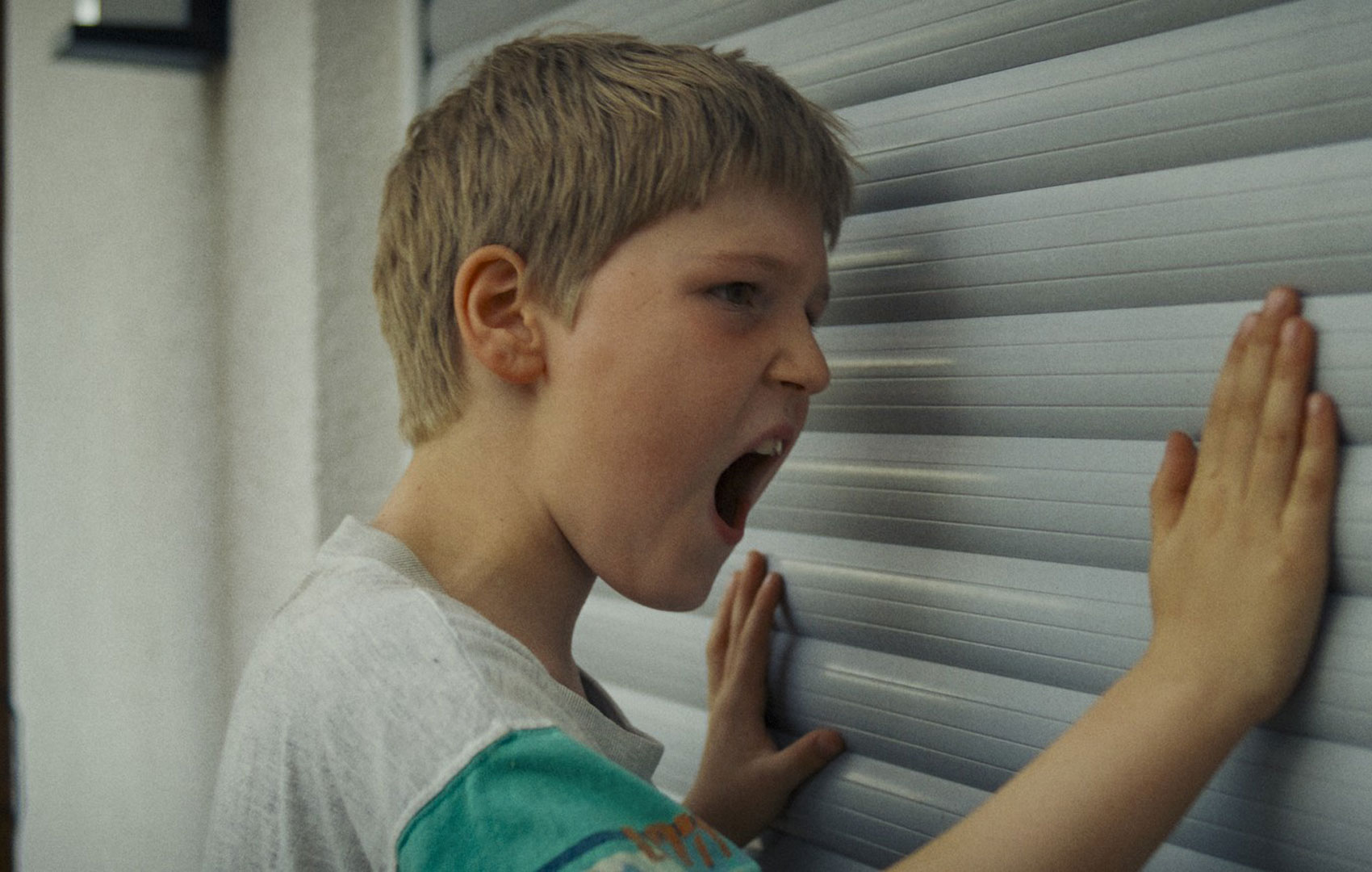 Ein Junge schreit und schlägt mit flachen Händen von außen gegen einen Rolladen.