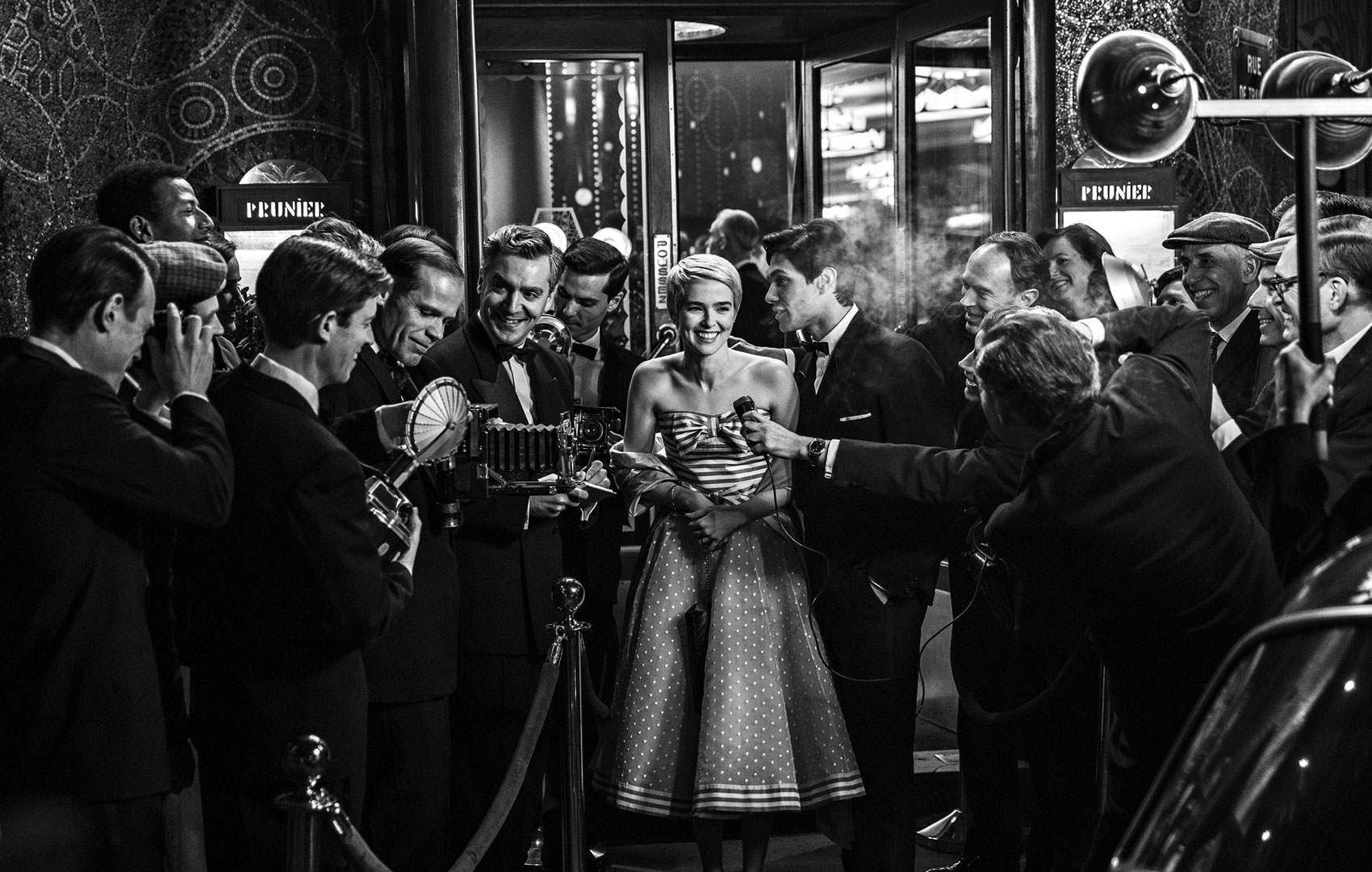 Schwarz-weiß Bild: Ein Frau wird auf der Straße vor einem Gebäude interviewt. Sie ist umringt von Journalisten, Kameras und Mikrofonen.