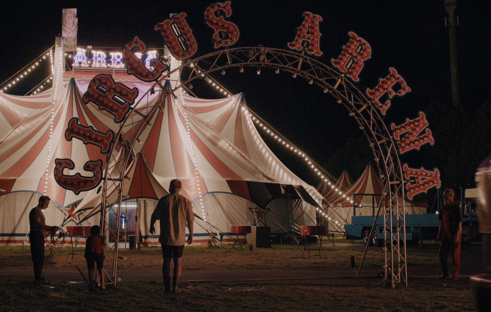 Im Hintergrund wird ein Zirkuszelt aufgebaut. Im Vordergrund steht in großen Lettern Circus Arena über dem Eingangstorbogen.